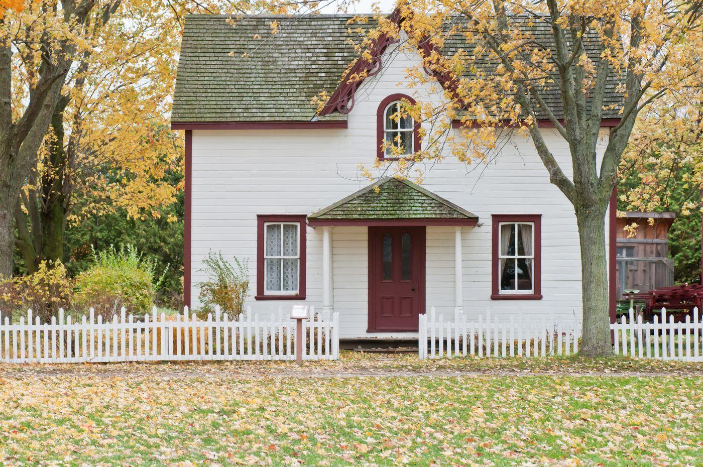 A two-story house with a white picket fence on a tree-lined Syracuse street